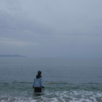 Bild aus dem Film "Uncontained", auf dem eine Person im Meer steht und in Richtung des Horizontes blickt