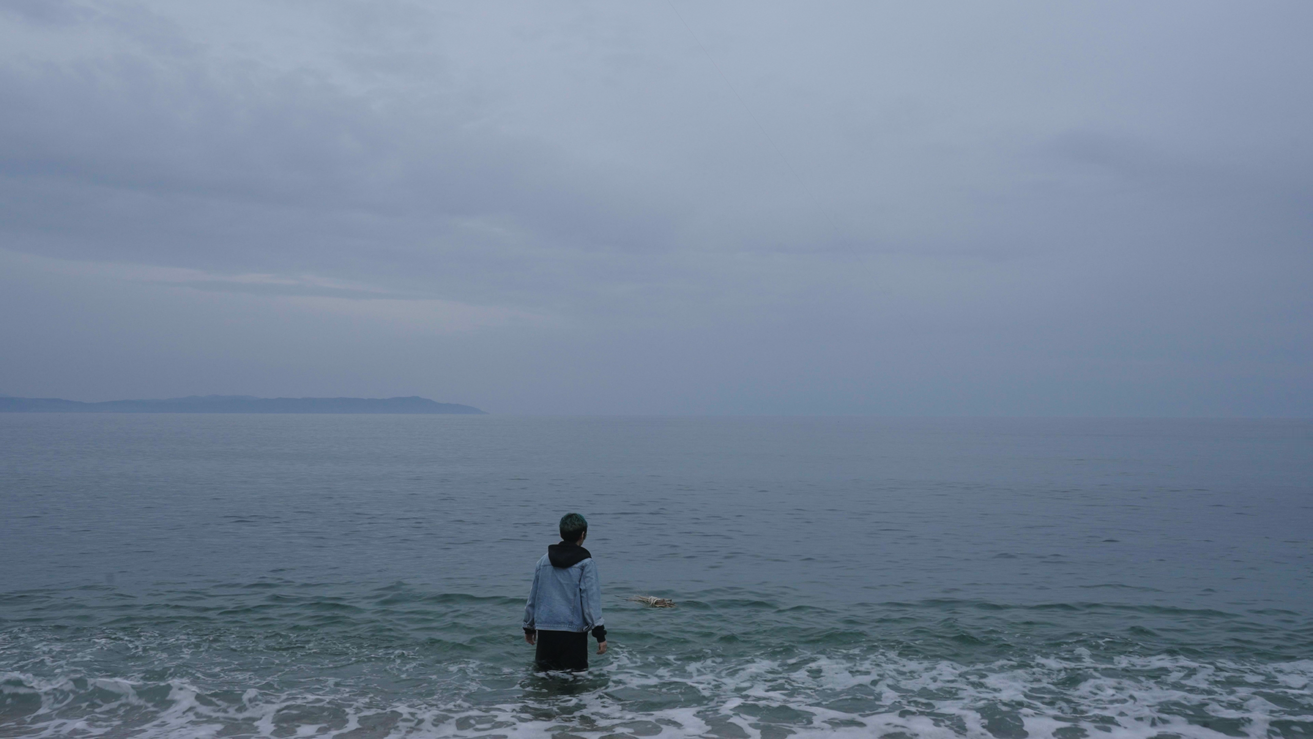 Bild aus dem Film "Uncontained", auf dem eine Person im Meer steht und in Richtung des Horizontes blickt